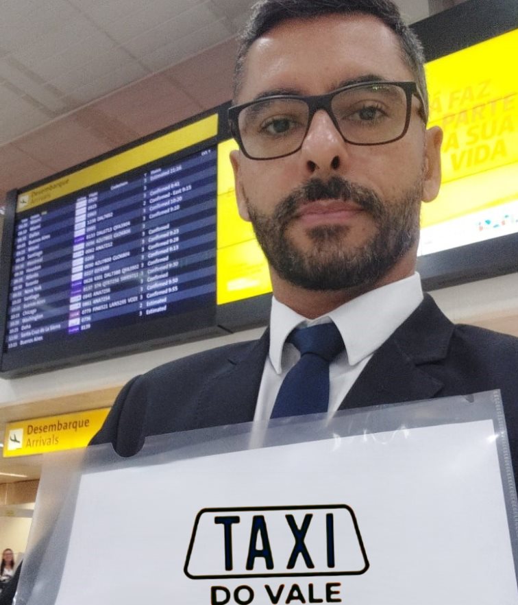 Motorista do Táxi do Vale recebendo clientes no aeroporto com placa