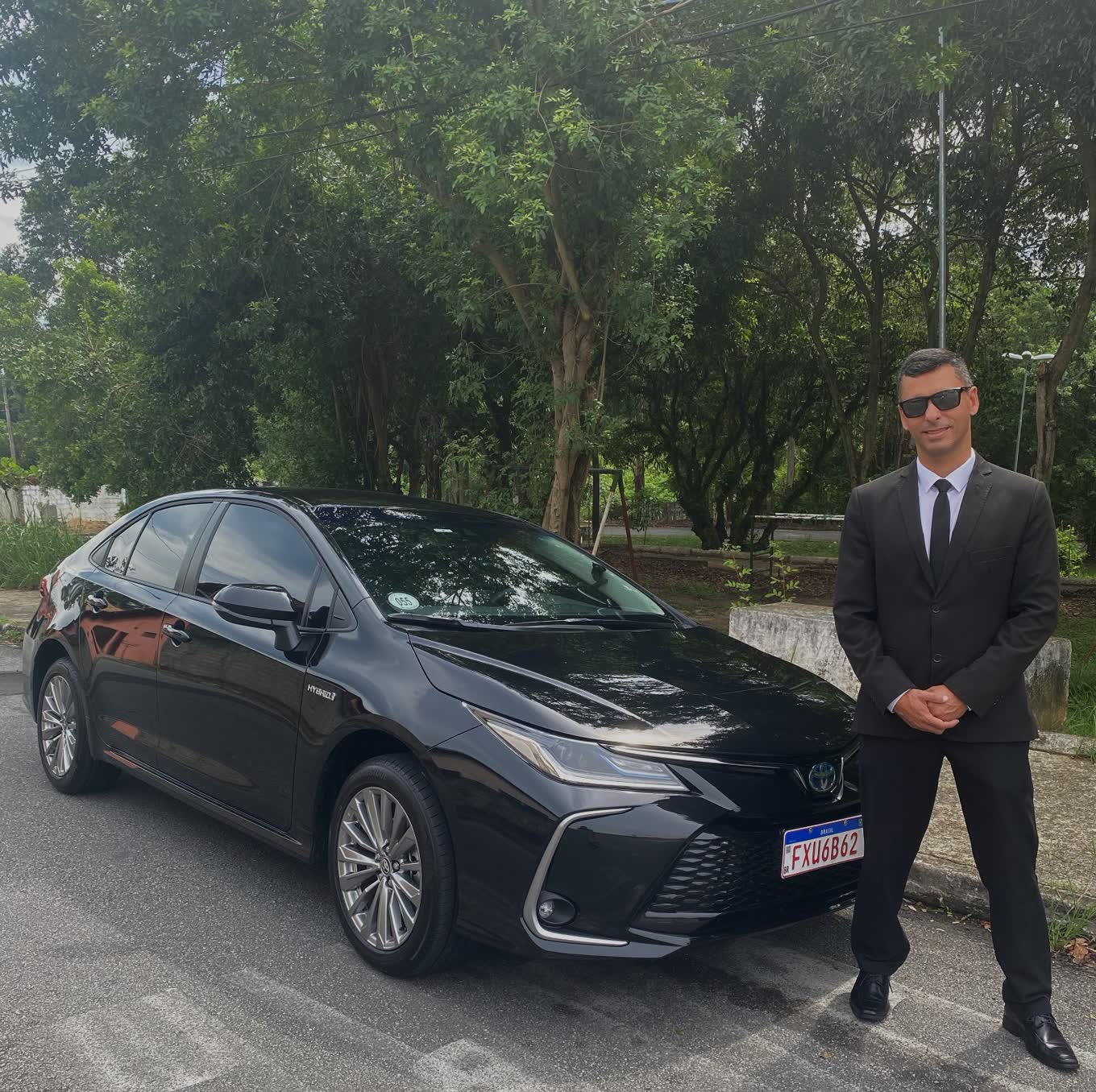 Motorista do Táxi do Vale de terno ao lado do sedã executivo preto